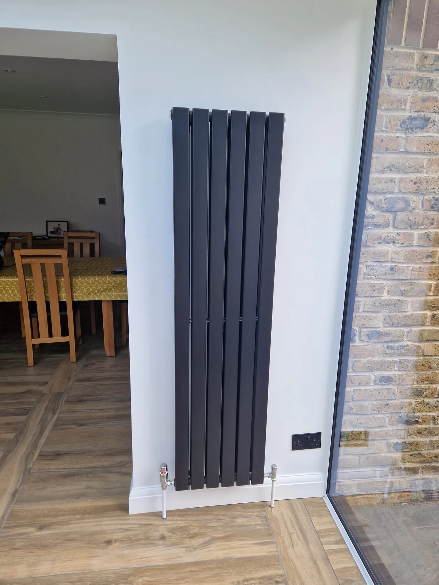 Tall vertical designer radiator installed beside a patio door in Romford